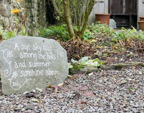 Front garden featuring a stone engraved with the words: A soft sky was among the hills and summer sunshine above.
