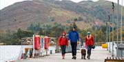 Visitors and a Dog walk along a pier on Ullswater in the Lake District, Cumbria