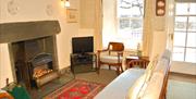 Lounge with open fire built with slate from the local quarry, electric fire, window and door to the front in Wistaria Cottage in Elterwater, Lake Dist