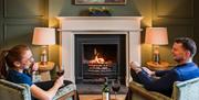 Guests relaxing by the fire with wine at The Borrowdale Hotel in Borrowdale, Lake District