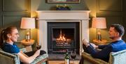 Guests relax by the fire with wine at The Borrowdale Hotel in Borrowdale, Lake District