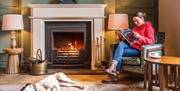 Guest and dog relax by the fire with a magazine at The Borrowdale Hotel in Borrowdale, Lake District