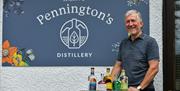 Mike Pennington posing with Pennington's Spirits in front of the sign for the distillery in Kendal, Cumbria © Christopher Holmes Photography