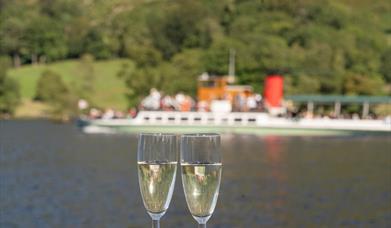 Two glasses of prosecco with an Ullswater 'Steamer' in the background