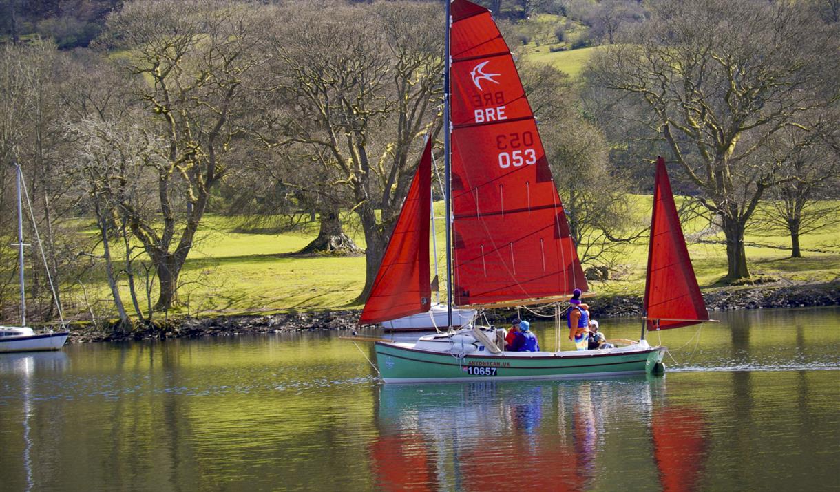 Sailing Boat with red sail backlit by the green fields