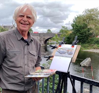 Kendal based artist Bob Henfrey and a Painting, Standing Riverside in Kendal, Cumbria