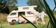 Macro Photo of Blades of Grass, with Visitors Unpacking a Caravan in the Background at Moss Howe Farm Campsite in Witherslack, Lake District