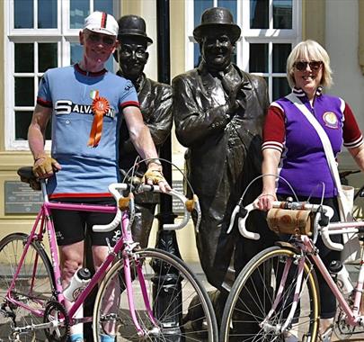 Visitors at the Velo Retro Vintage Cycling Event, posing with the Laurel and Hardy Statue in Ulverston, Cumbria