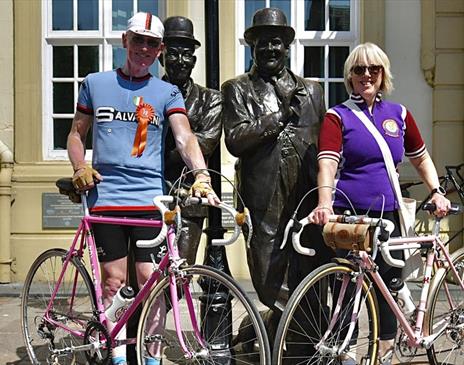 Visitors at the Velo Retro Vintage Cycling Event, posing with the Laurel and Hardy Statue in Ulverston, Cumbria