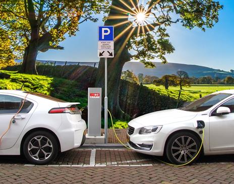 Two electric vehicles charging in a car park with a scenic backdrop
