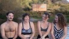 Image shows 4 people in Llyn Padarn with the sauna in the background