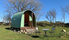 A green hut in the north Wales sunshine. Outside are a table and chairs. The sky is blue.