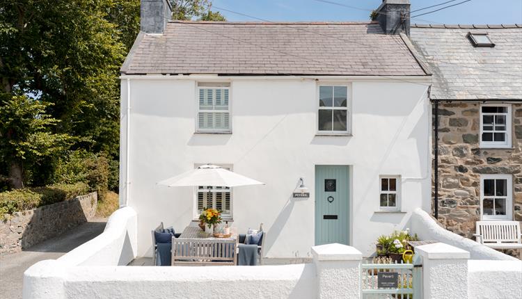 Traditional whitewashed cottage with a private walled courtyard, outdoor dining table and parasol, beside a quiet village lane.