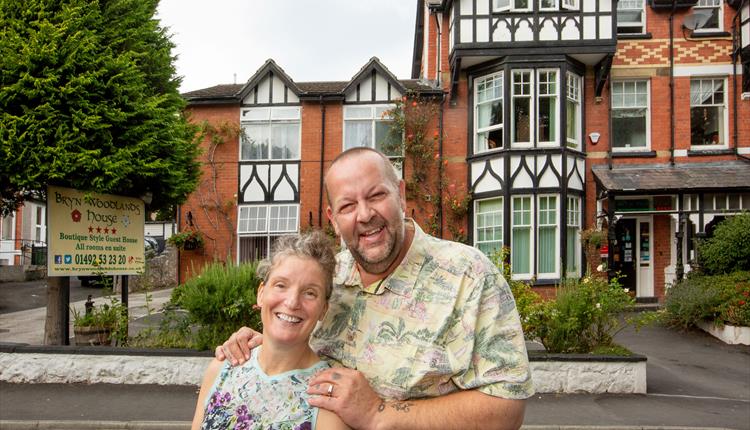 This image shows the owners Tracey and Joel in front of the mock Tudor triple height Victorian building with black and white features.  Plants growing