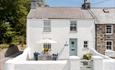 Traditional whitewashed cottage with a private walled courtyard, outdoor dining table and parasol, beside a quiet village lane.
