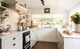 Light-filled kitchen with cream cabinetry, open shelving, farmhouse sink and large windows overlooking greenery outside.