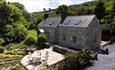 Traditional stone cottage surrounded by landscaped gardens, with a circular patio dining area and rolling hillside scenery beyond.