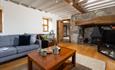 Characterful living room with exposed ceiling beams, a large stone fireplace, wood-burning stove, comfortable seating and wooden flooring.