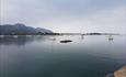 This image shows a calm sea with boats bobbing away and a grey cloudy sky