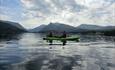 Breathtaking view of Llyn Padarn Lake with kayakers in green sit-on-top kayaks enjoying the water. The lush landscape of North Wales and the towering