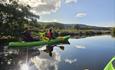 Serene view of green sit-on-top kayaks gently floating on the calm waters of Llyn Padarn Lake, North Wales, with perfect reflections of the kayaks in