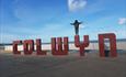 This image shows the Colwyn Sign built on the sea front with someone stood on the top of the Y with Blue sky and clouds