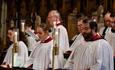 Bangor Cathedral choir in red and white robes, standing near brass candlesticks and singing at a service