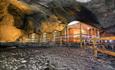 A wide shot of a chamber within a slate mine, four wooden Cabins for accommodation and a communal area.
