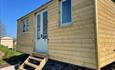 Front view of shepherd hut that has two windows and shows steps that lead up to front door.