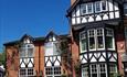 This image shows a mock Tudor triple height Victorian building with black and white features.  Plants growing up the walls and a gorgeous blue sky