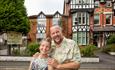 This image shows the owners Tracey and Joel in front of the mock Tudor triple height Victorian building with black and white features.  Plants growing