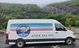 Paradise adventures van with bright colours and signwritting across it, in the national slate museum carpark with vivian quarry in the background