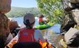 Adventurous group navigating through a shadowy tunnel in green sit-on-top kayaks on Llyn Padarn Lake, North Wales. The kayakers, wearing red buoyancy