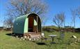 A green hut in the north Wales sunshine. Outside are a table and chairs. The sky is blue.