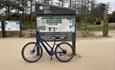 Photos of bike leaning against signage in Newborough Forest of the walking and cycle routes,