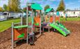 Play area surrounded by caravans. slide and climb options with bark chip safety floor