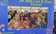 A family of four adults and two children behind the Mold Food and Drink photo frame which is blue and has the Mold Food and Drink logos and social med