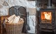 The woodburning stove at Gors-lwyd Cottage with a supply of logs in the log basket