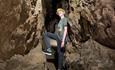 A young teen standing in a narrow underground tunnel, leaning against the wall and resting his foot on the rock in front of him.