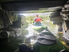 Adventurous group navigating through a shadowy tunnel in green sit-on-top kayaks on Llyn Padarn Lake, North Wales. The kayakers, wearing red buoyancy