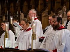 Bangor Cathedral choir in red and white robes, standing near brass candlesticks and singing at a service