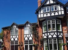 This image shows a mock Tudor triple height Victorian building with black and white features.  Plants growing up the walls and a gorgeous blue sky