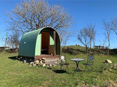 A green hut in the north Wales sunshine. Outside are a table and chairs. The sky is blue.