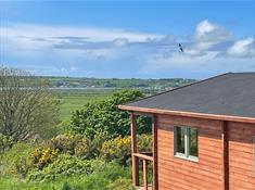 Blue sky with a swallow flying above the log cabin which looks out towards the sea.