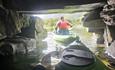 Adventurous group navigating through a shadowy tunnel in green sit-on-top kayaks on Llyn Padarn Lake, North Wales. The kayakers, wearing red buoyancy