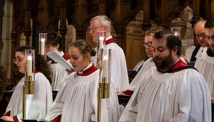 Bangor Cathedral choir in red and white robes, standing near brass candlesticks and singing at a service