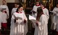 Bangor Cathedral choir in red and white robes, with two members of the choir sharing a joke.