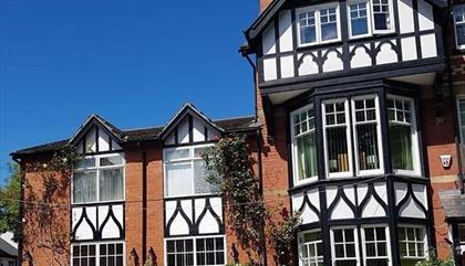 This image shows a mock Tudor triple height Victorian building with black and white features.  Plants growing up the walls and a gorgeous blue sky