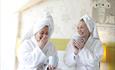 This image shows two women with towels on their heads like the have just showered and having a cuppa both laughing