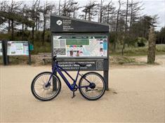 Photos of bike leaning against signage in Newborough Forest of the walking and cycle routes,